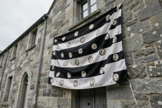 Drapeau breton Gwenn ha Du avec les onze hermines accroché sur une façade en granit breton